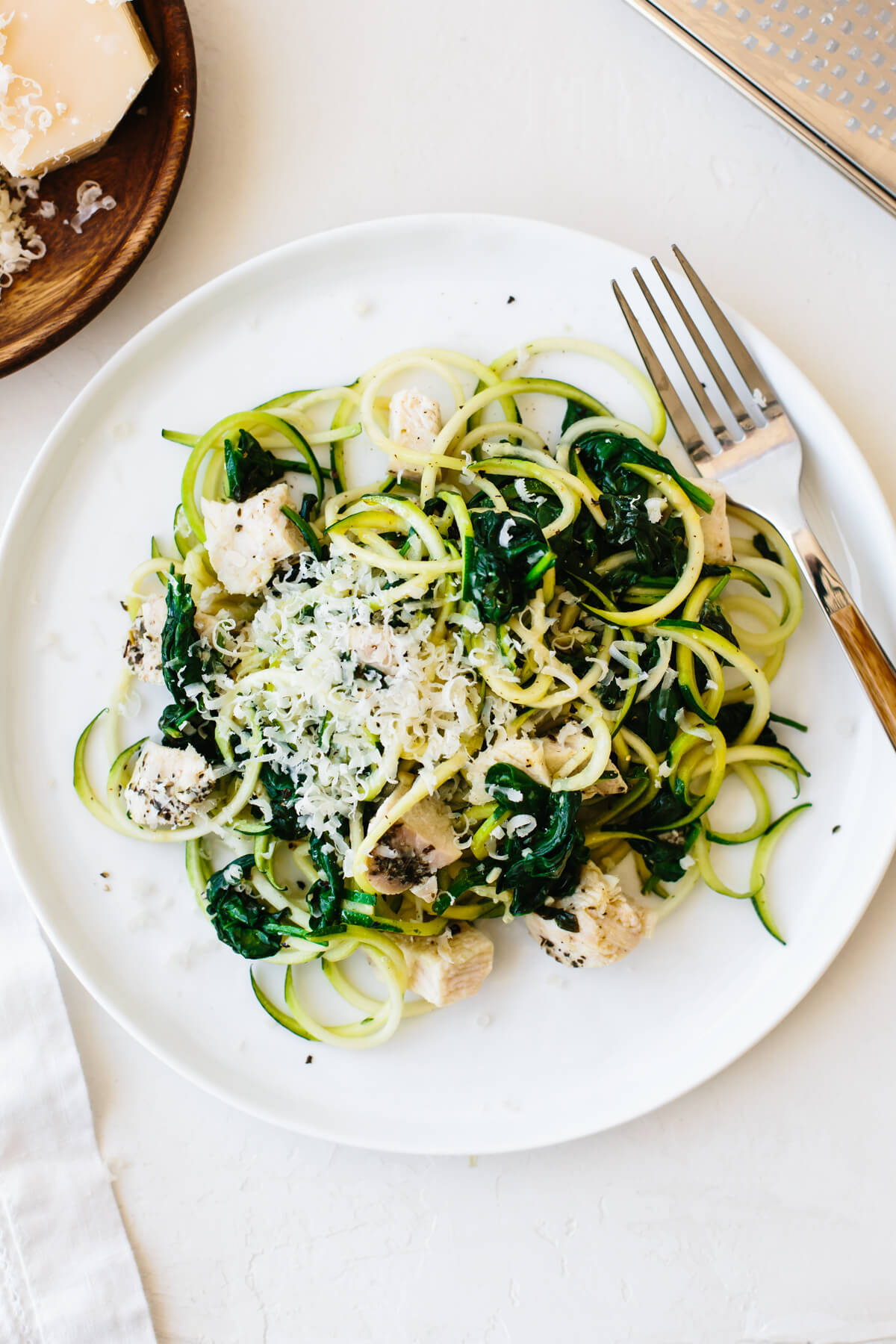 Un plato de fideos de calabacín con trozos de pollo, espinacas salteadas y un espolvoreado de parmesano.